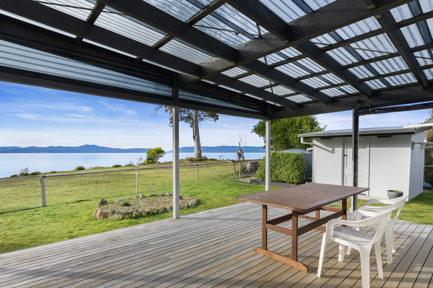 Covered timber deck with dining table looking out over the lawn and bay