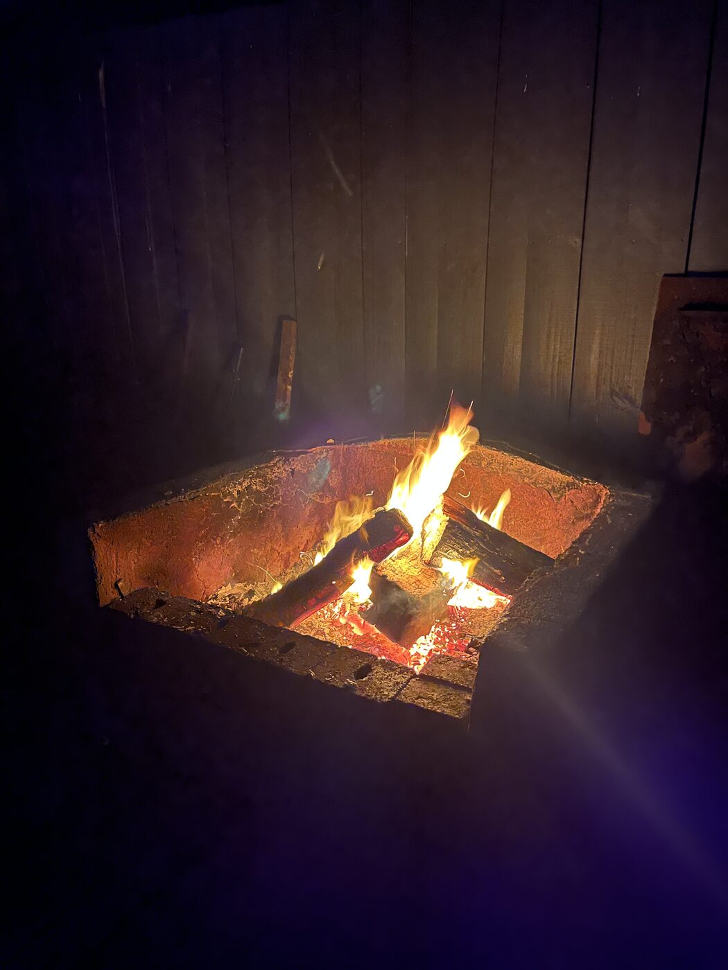 Outdoor firepit burning at night against a timber fence