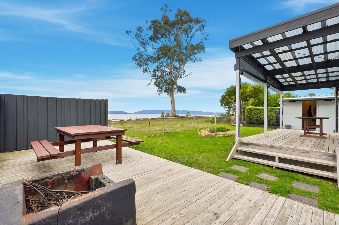 Firepit and picnic table on the deck, looking past the lawn to the bay